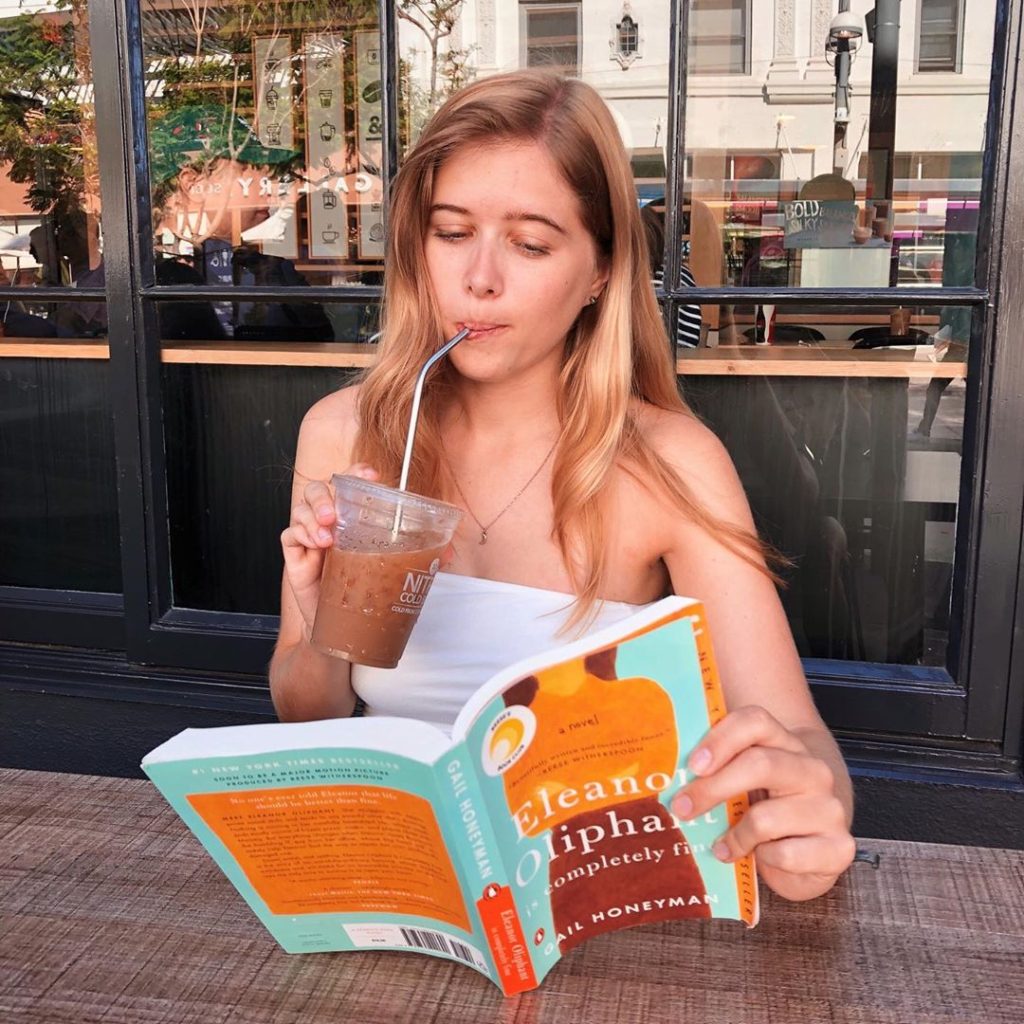 Book blogger drinking a Peet's iced coffee and reading Eleanor Oliphant is Completely Fine by Gail Honeyman, in Los Angeles, California.
