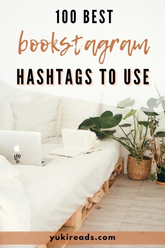 Aesthetic white boho bedroom with plants and a Mac laptop next to a pile of books with text overlay that says 100 best Bookstagram hashtags to use